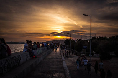 People by sea against orange sky