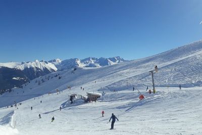 People skiing on snowcapped mountain against blue sky