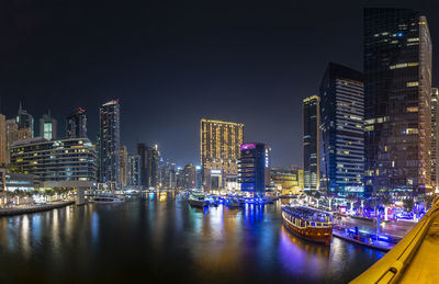 Illuminated buildings by river against sky in city at night