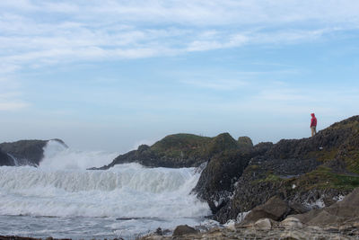 Scenic view of sea waves splashing on rock formations against sky