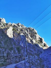 Low angle view of rocky mountain against clear blue sky