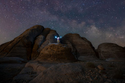 A man holding light at night on a rock canyon facing the milky way