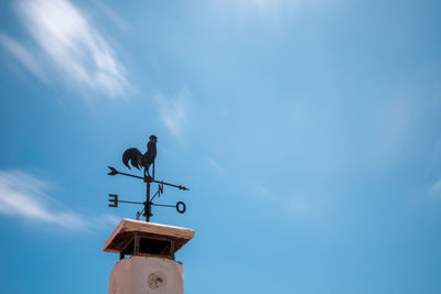 Low angle view of weather vane against blue sky