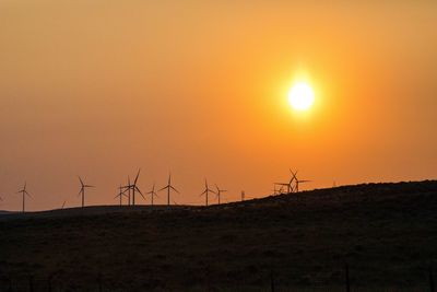 Silhouette of wind turbines on land during sunset