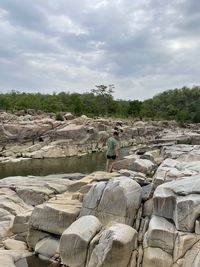 Rear view of man standing on rock against sky