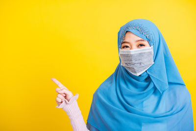 Portrait of young woman wearing mask against yellow background