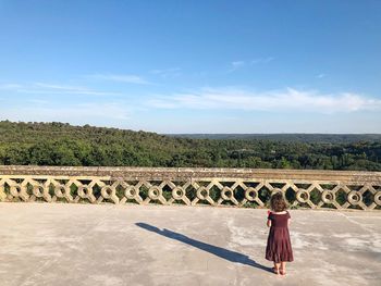 Rear view of girl standing on building terrace against sky