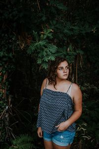 Young woman looking away while standing against plants in forest