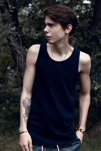 Young man with tattoo on arm looking away while standing against trees