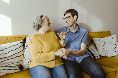 Happy man with arm around senior mother-in-law sitting on sofa at home