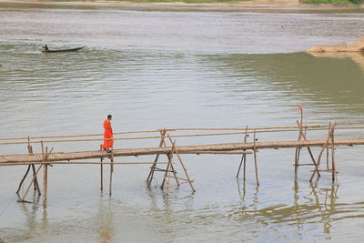 Reflection of buddhist monk walking on bamboo bridge