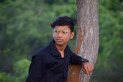 Portrait of young man standing by tree trunk