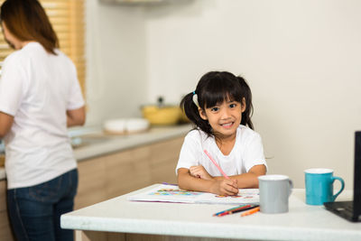 Portrait of girl painting on table with mother in background