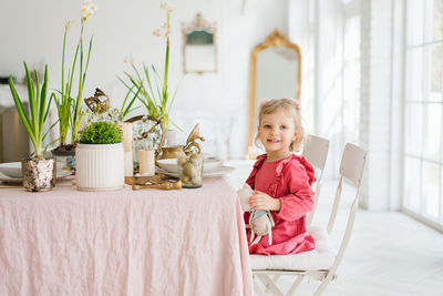 Little girl in a pink dress is sitting at the easter table for a festive breakfast