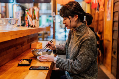 Side view of young woman holding food on table