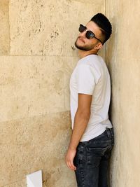 Young man wearing sunglasses while standing against wall