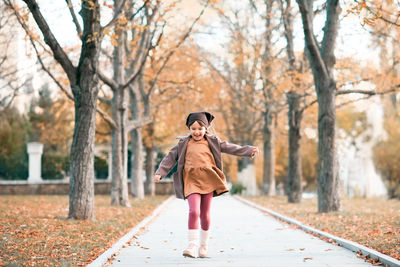 Happy smiling child 4-5 year old wear jacket and hat in park with fall leaves over nature background