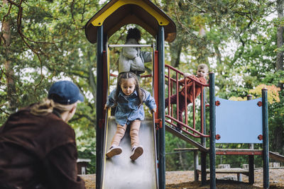 Male teacher looking at girl playing on slide in playground