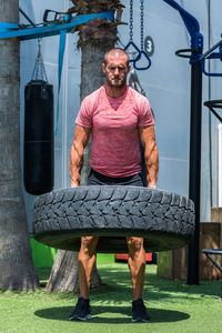 Muscular focused male athlete lifting heavy tire during active functional workout on sports ground