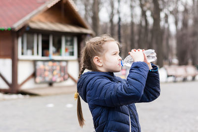 Cute little girl drinks water from a bottle on the background of a food truck in a city park