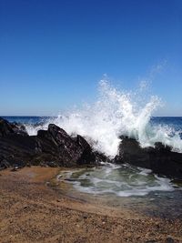 Waves splashing on sea against clear blue sky