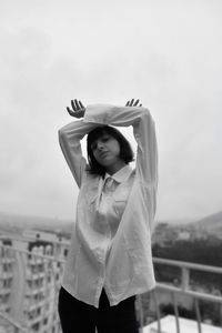 Portrait of young woman standing at balcony against sky