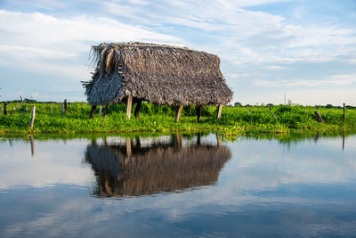 Hut on land by lake against sky