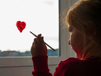 Little girl holds paintbrush in hand drawing heart on window valentine's day love dating quarantine 