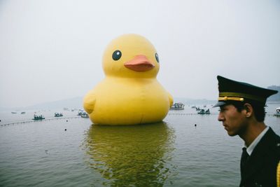 Man with yellow bird in water against sky