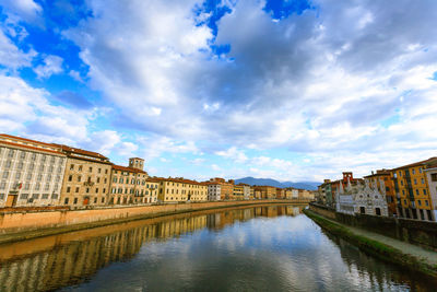 Canal passing through buildings against cloudy sky