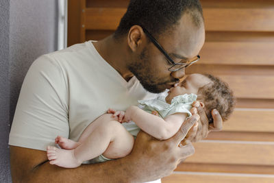 Father kissing cute baby girl in front of wooden wall