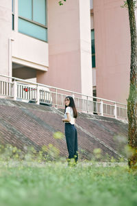 Portrait of young woman standing on grass in front of building at park