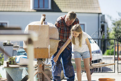 Grandfather using cement mixer with granddaughter in yard