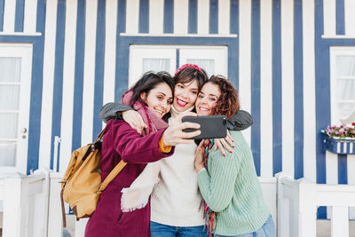 Happy women friends using mobile phone in front of colorful houses.costa nova, aveiro, portugal