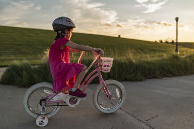 Side view of girl learning to ride bicycle on road against sky