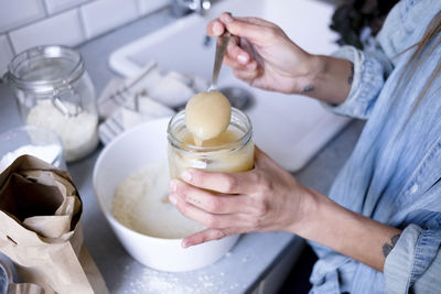 Midsection of woman adding ingredient in bowl at kitchen counter