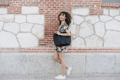 Full length portrait of woman standing against brick wall