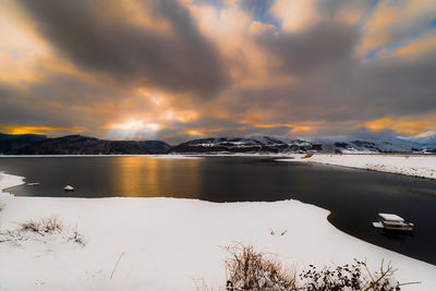 Scenic view of lake by snowcapped mountains against sky during sunset