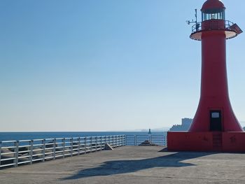 Lighthouse by sea against clear sky