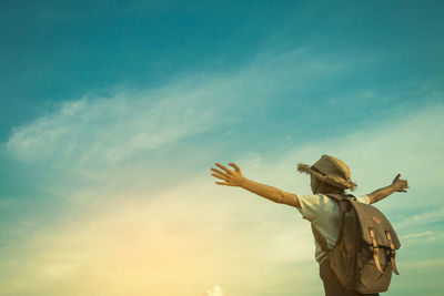 Low angle view of schoolgirl with arms outstretched standing against cloudy sky