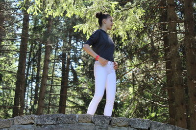 Side view of young man standing against trees in forest