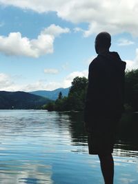 Rear view of man looking at lake against sky