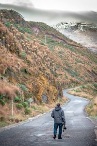 Rear view of man walking on road against mountain