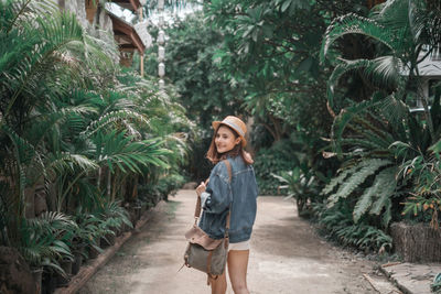 Portrait of smiling young woman standing on footpath amidst plants