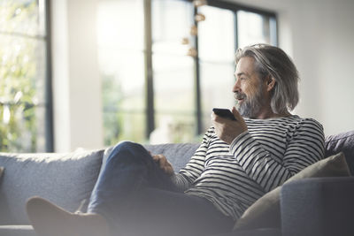 Senior man sitting on couch, using smartphone