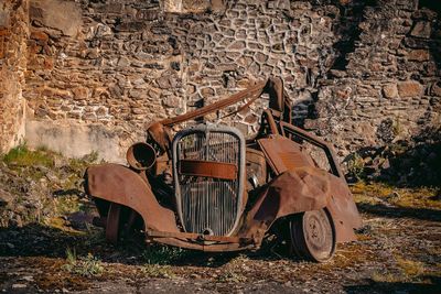 Abandoned car on field against stone wall