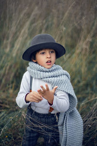 Boy child in plaid pants, hat, suspenders and scarf stands in a field in autumn