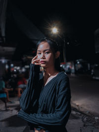 Portrait of beautiful young woman standing on street at night