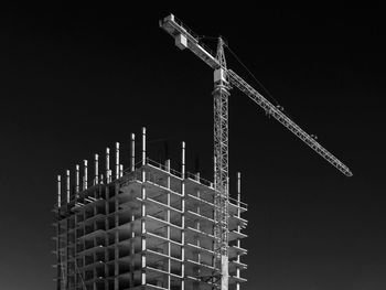 Low angle view of crane by incomplete building against sky