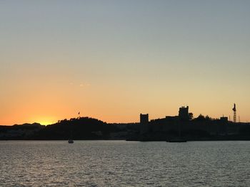 Silhouette buildings by sea against sky during sunset